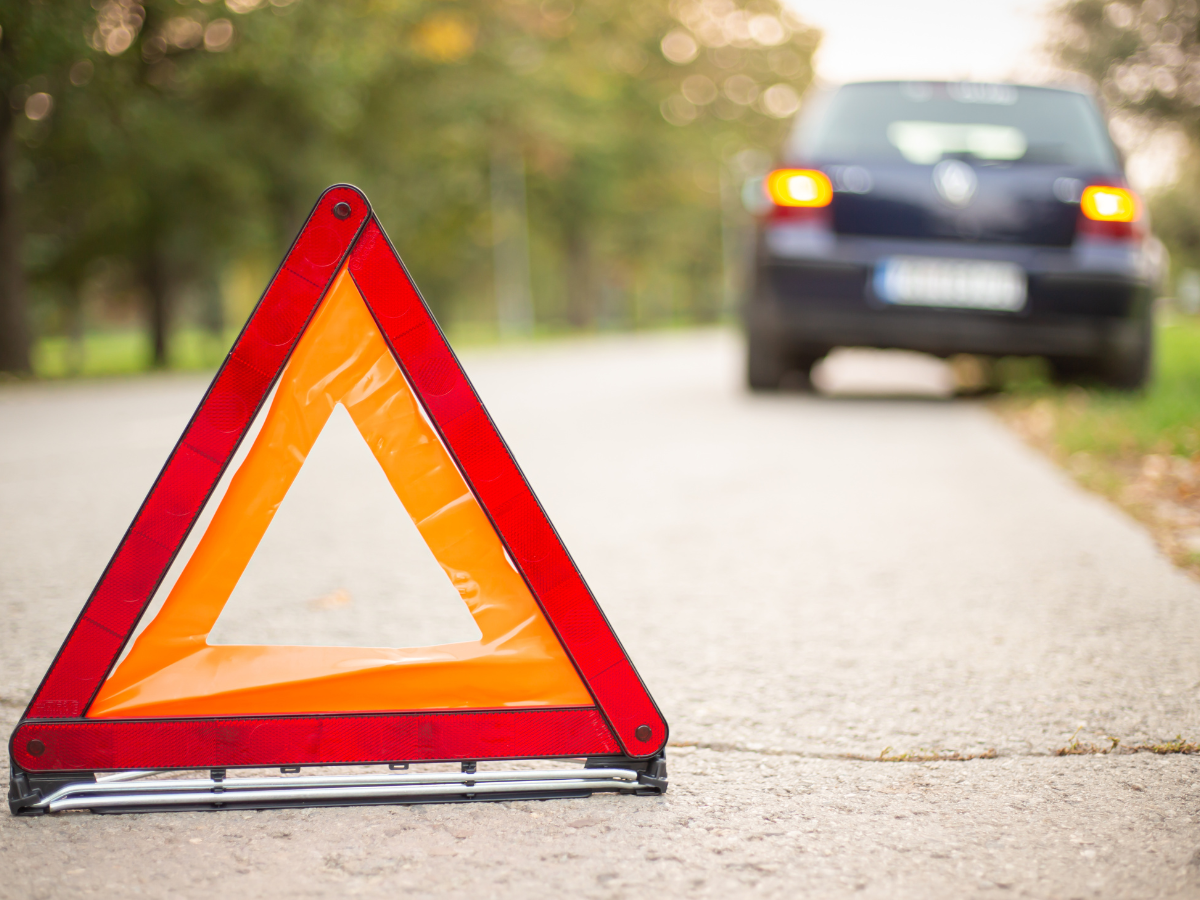 A cone in the road and up ahead a car is pulled over to the side.